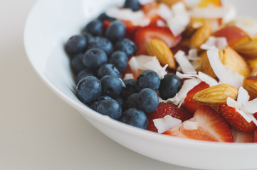 Plate with fresh blueberries, sliced strawberry, banana, peach, coconut flakes and almond. Healthy and balanced breakfast