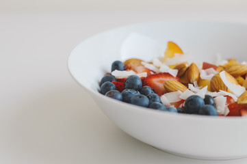 White plate with healthy and balanced breakfast meal. Fruit mix: blueberry, peach, banana, almond, strawberry and coconut flakes