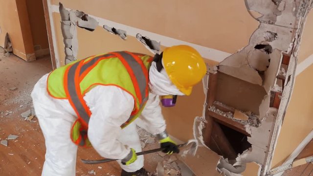 Worker in protective suit demolishes plaster wall. (with Audio)