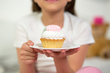 Charming little girl holding cake on plate. Yummy cupcake with white icing being held by cute little girl on white ceramic plate.