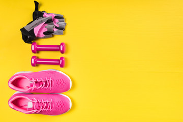 pink sneakers, dumbbells and sport gloves lie in a row on a yellow background