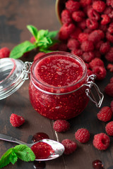 fresh raspberry jam in a glass jar on a wooden table, next to fresh raspberries and mint leaves. concept of homemade jam, preparation for winter, selective focus and copy space