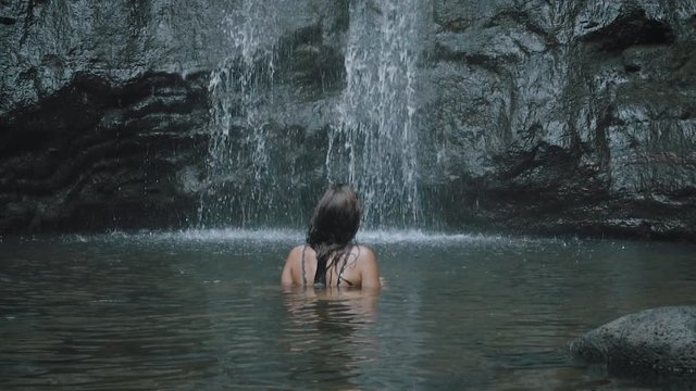 Slow motion model standing up and relaxing under tropical waterfall in Hawaii.