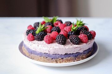 Raw vegan cake with raspberries and bluberries on white table