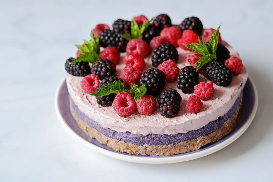 Raw vegan cake with raspberries and bluberries on white table