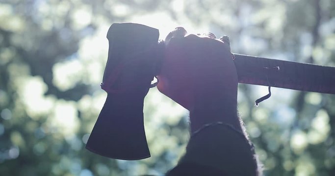 Male hand holds an ax on the forest background. Close-up lumberjack in the forest with an ax in his hands