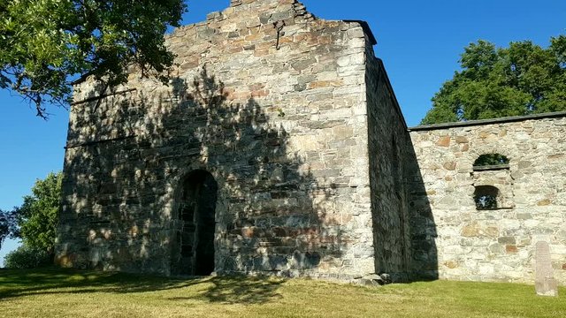 Old church ruin Nes Kirkeruiner entrance summer day with trees and gravestone