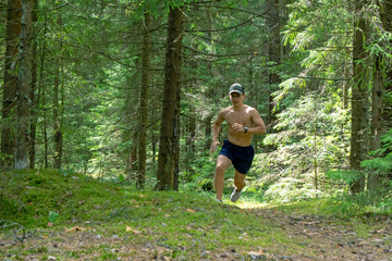 Athlete, a teenager with a bare torso, shorts and a cap running in the forest marathon distance