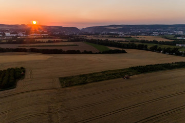 Aerial view of combine harvester harvesting an oats crop at sunset