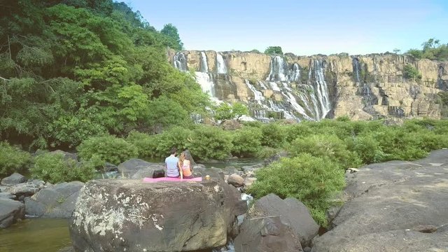 camera moves past guy girl sitting on stone to waterfall