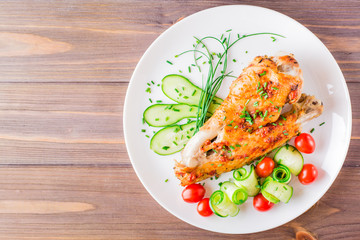 Baked in a spices turkey wing, cucumber slices and cherry tomatoes on a plate on a wooden table. Top view