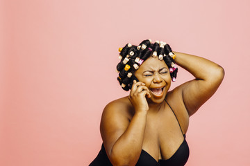 Woman with hair curlers and neglige laughing while talking on phone, isolated on pink
