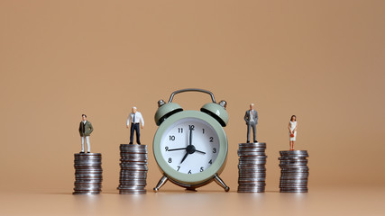 The miniature people standing on piles of coins and an alarm clock.