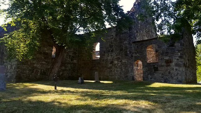 Nes Kirkeruiner pedistal from the grass up in the air showing old stone church ruins, trees and gravestones