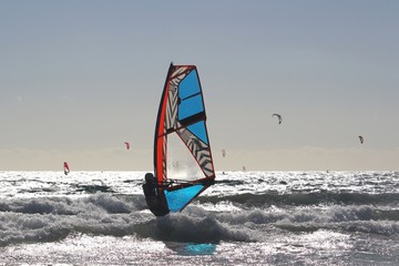 Windsurfer among the shore break of the Atlantic ocean glistening in the sun, in back light