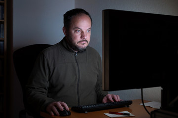 middle aged man sitting in front of computer screen in the dark