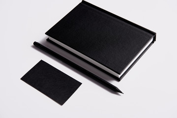 isometric view of black notebook with pencil and business card on white tabletop for mockup
