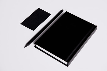 isometric view of black notebook with pencil and business card on white surface for mockup