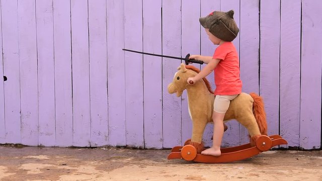 Funny child in old military cap with red star, on toy horse-rocking horse with plastic sword. Boy dreams of battles, victories and adventures. concept of preparation of  moral spirit, education