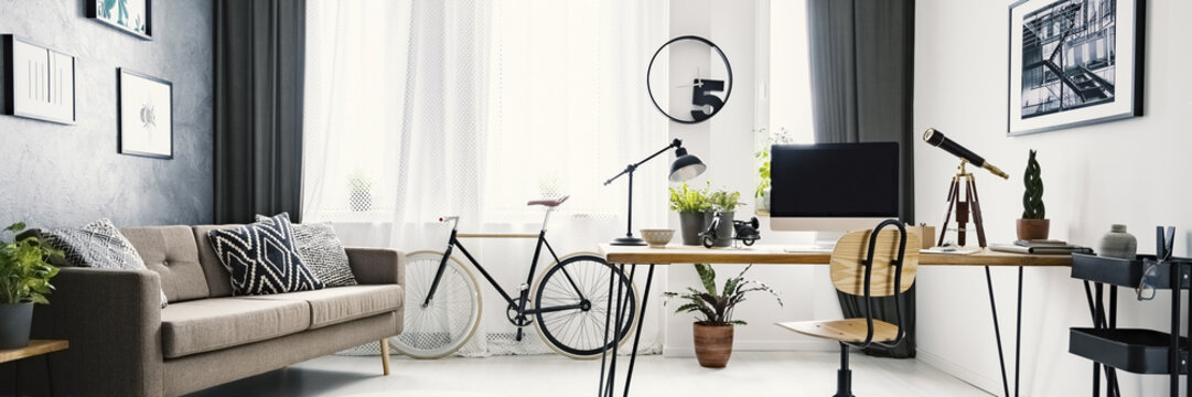 An urban bicycle in a hipster living room interior with a big desk and computer in the workspace area and wooden furniture with industrial elements