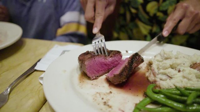 A man cutting rare stake with knife and a fork.