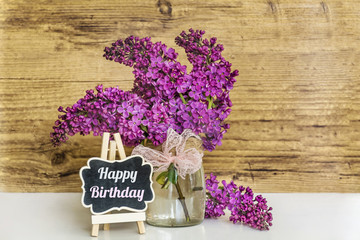 Spring Bouquet of Lilac with Pink Ribbon and Happy Birthday Message on a Wooden Background