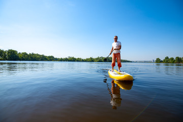 Joyful man paddling on a SUP board and enjoying life