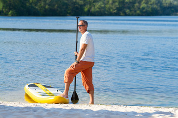Happy man with a paddle stands next to SUP board