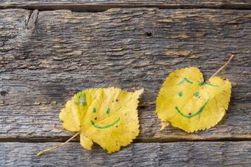 Yellow autumn leaves with smiley patterns on wooden background.