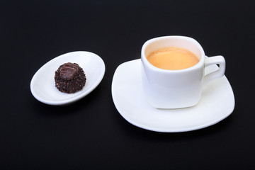 White cup of classic espresso coffee and pralines on black background.