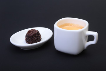 White cup of classic espresso coffee and pralines on black background.