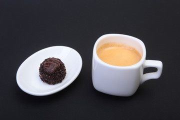 White cup of classic espresso coffee and pralines on black background.