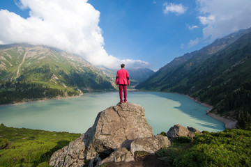 businessman in a red suit on top of a mountain in the background of a mountain lake,Big Almaty Lake