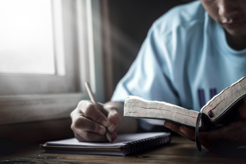 Young man reading Holy Bible and writing note book.