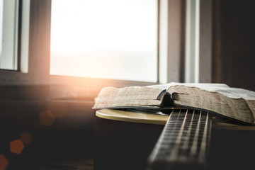 Open Holy Bible on acoustic guitar with sunlight background.