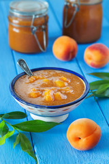 Bowl of apricot jam with spoon and fruit on blue table