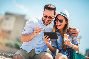 Happy couple paying on line with credit card and digital tablet on the street