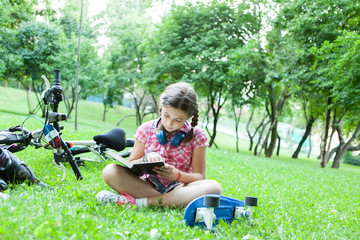 Fototapeta premium Girl reading a good book in the park next to her bicycle 