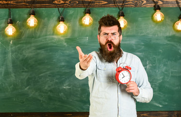 Schedule and regime concept. Teacher in eyeglasses holds alarm clock. Man with beard on shouting...