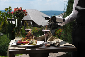 Romantic dinner outside. an appetizing dish of pork ribs and two glasses of red wine, green grass and flowers in the background.