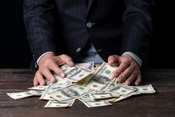 Pile of paper currency ..Man hands in pinstripe suit sweeping pile of US dollar banknotes on old...