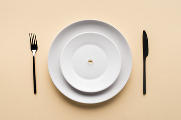 top view of black fork, knife and plate with one pill on beige background