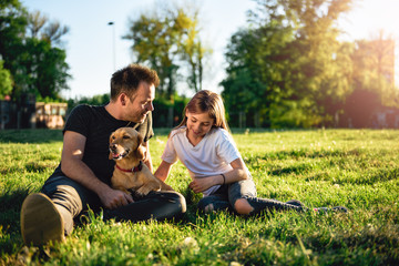 Father and daughter relaxing at park with dog