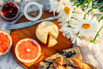 Fruits, croissants, jam, tea and flowers on tablecloth in summer sunlight. Picnic concept