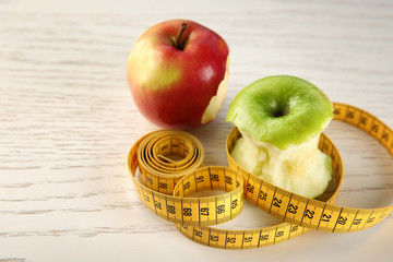 Bitten apples and measuring tape on wooden table. Diet food