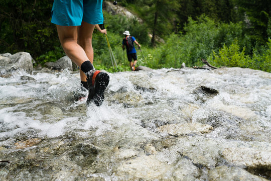 A trail runner crossing a stream while hiking through the Alps