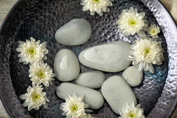 Fototapeta na wymiar Plate of water with flowers and stones prepared for pedicure treatment in spa salon, closeup