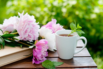 Fototapeta na wymiar Book and cup of tea on a wooden table with flowers, summer garden, concept of relaxation and reading