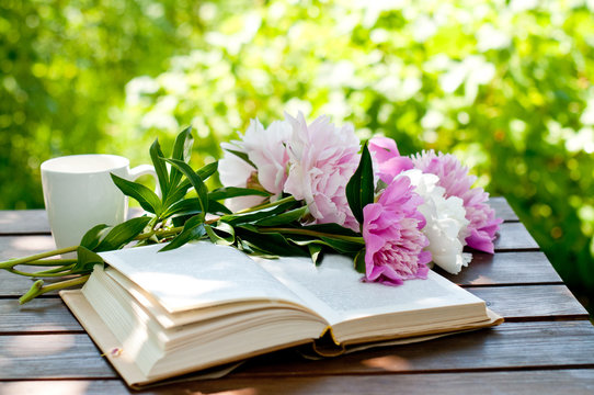 Book and cup of tea on a wooden table with flowers, summer garden, concept of relaxation and reading