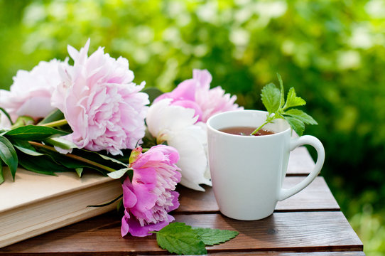 Book and cup of tea on a wooden table with flowers, summer garden, concept of relaxation and reading